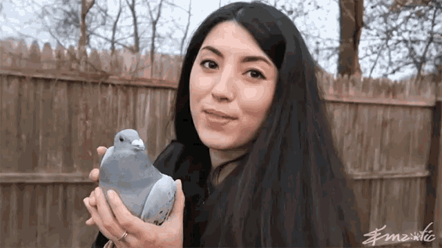 a woman is holding a pigeon in her hands with a fence in the background and a watermark that says fm2xtic