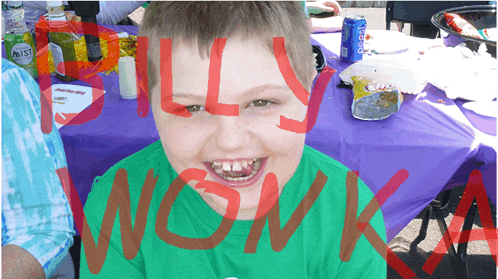 a boy in a green shirt is sitting at a table with a purple table cloth that says billy wonka on it