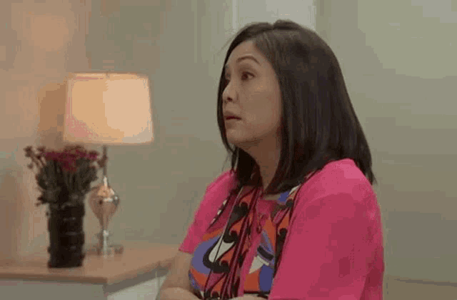 a woman in a pink shirt is sitting in a room next to a lamp .