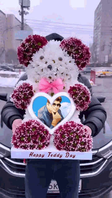 a man holding a teddy bear made of flowers with a picture of a man in a heart on it
