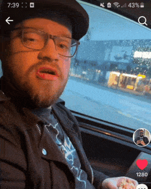 a man wearing glasses and a hat is sitting in a car with the time of 7:39 on his phone screen