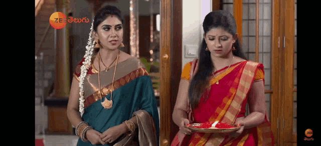 two women in saris are standing next to each other in a room holding plates of food .