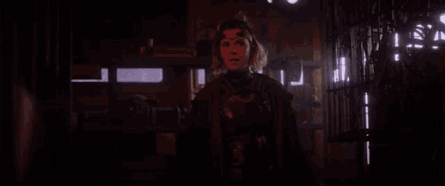 a woman in a costume is standing in a dark room with a cage in the background .
