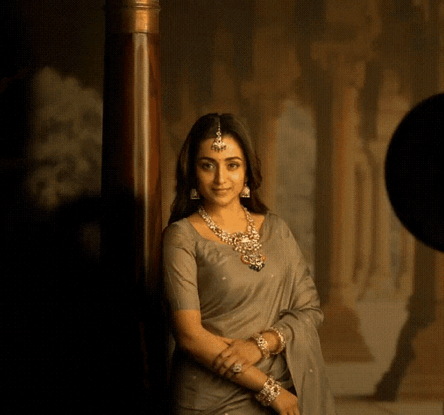 a woman wearing a necklace and earrings is leaning against a wall