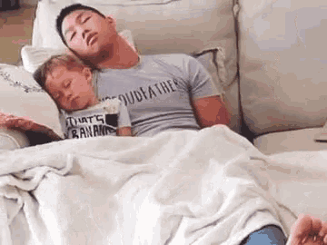 a man is sleeping on a couch with a baby on his lap .