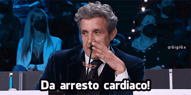 a man in a suit and tie says da arresto cardiaco while holding a microphone
