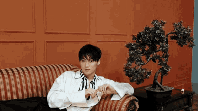 a man in a white shirt is sitting on a couch next to a potted plant