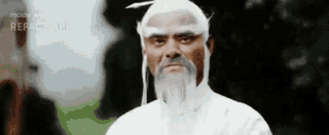 a man with a beard and white hair is wearing a white robe and looking at the camera .