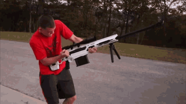 a man in a red shirt is holding a large rifle