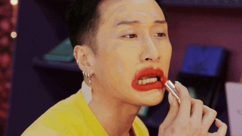 a man in a yellow shirt is applying red lipstick on his lips