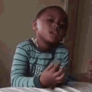 a young boy is sitting on a bed holding a cell phone in his hands .