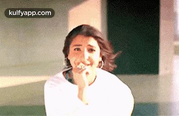 a woman in a white shirt is making a funny face while holding her hand to her mouth .