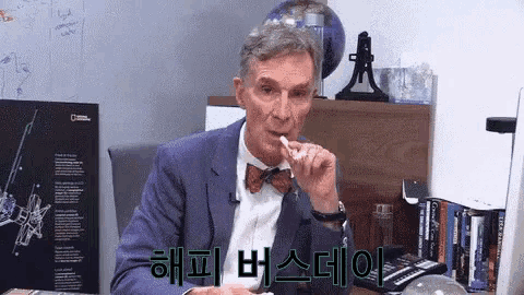 a man in a suit and bow tie is sitting at a desk and eating a candy bar .