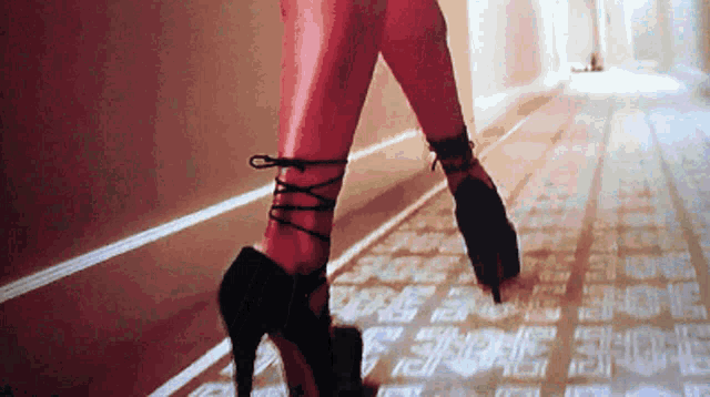 a woman is walking down a hallway wearing a pair of black high heels