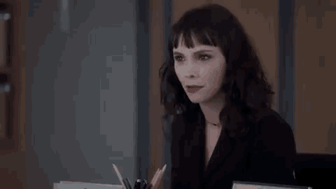 a woman is sitting at a desk with a pen holder and smiling at the camera .