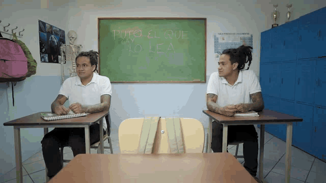 two students sit at their desks in front of a chalkboard that says puto el que lo lea