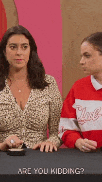 two women are sitting at a table and one of them is wearing a red and white sweater that says club