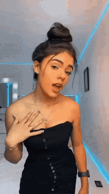 a woman in a black dress is standing in a room with a bun in her hair .