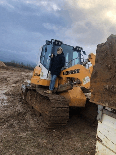 a woman leans against a liebherr bulldozer in a muddy field