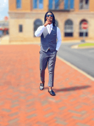 a man in a suit is standing on a brick sidewalk with his hands in his pockets