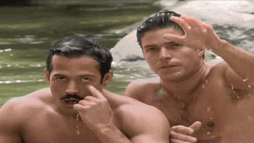 two shirtless men are standing next to each other and one is pointing at his eye