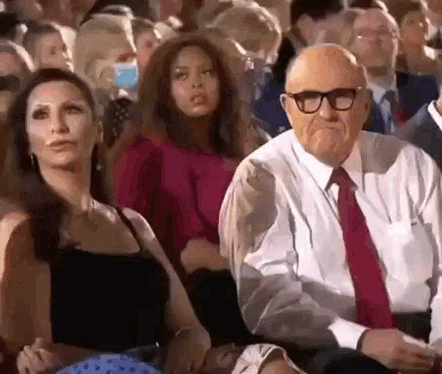 a man and a woman are sitting in a crowd of people wearing masks .