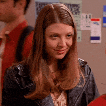 a woman in a leather jacket stands in front of a bulletin board with a poster that says " let 's go "
