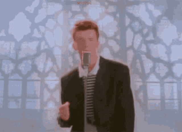 a man in a suit singing into a microphone while wearing glasses and a striped shirt