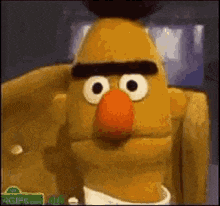 bert from sesame street is wearing a white shirt and tie while sitting on a chair .