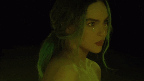 a close up of a woman with green hair and a tear on her face .