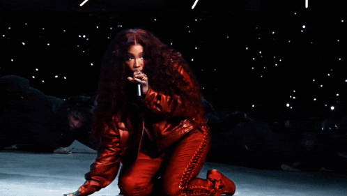 a woman in a red jacket is singing into a microphone while kneeling down