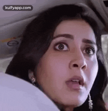 a woman is sitting in the back seat of a car making a surprised face .
