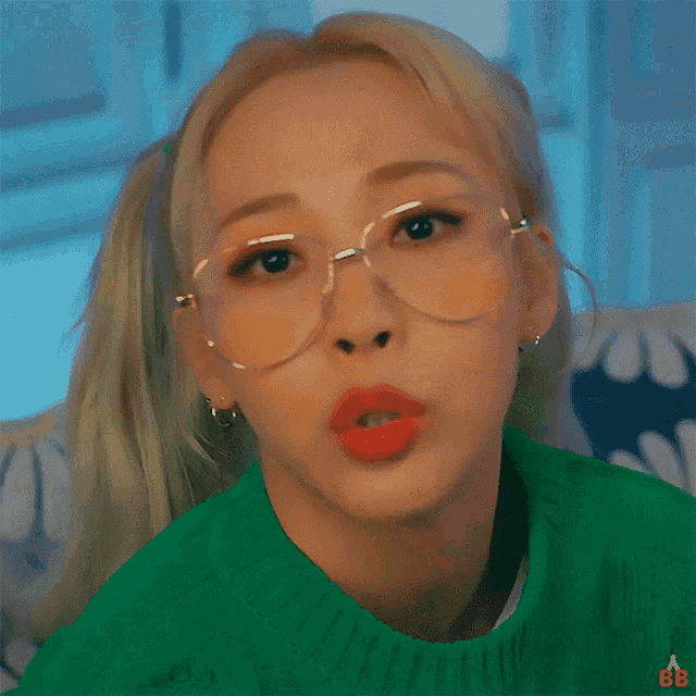 a close up of a woman wearing glasses and a green sweater with the letters bb on it