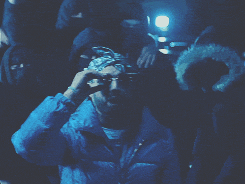 a man wearing sunglasses and a bandana stands in a crowd of people