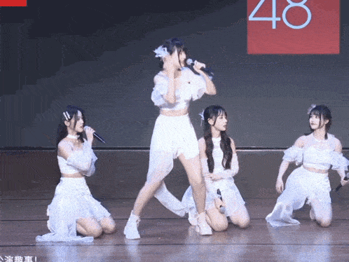 a group of girls are performing on a stage with the number 48 in the background