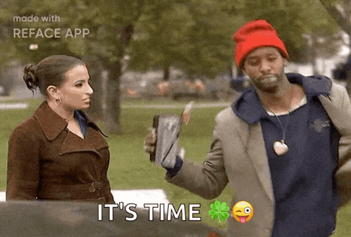 a man in a red hat is talking to a woman in a park while holding a book .