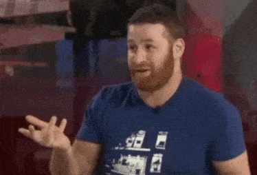 a man with a beard wearing a blue t-shirt is talking to someone .