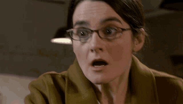 a woman wearing glasses and a brown coat looks surprised