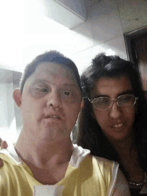 a man and a woman are posing for a picture together . the man is wearing glasses and a yellow shirt .