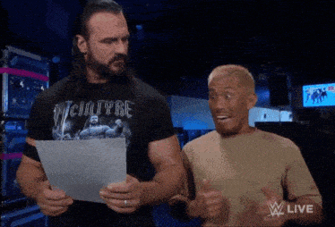 a man in a victoryre shirt holds a piece of paper in front of another man