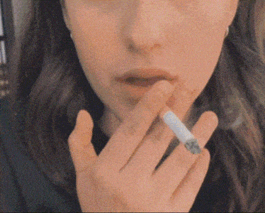 a close up of a woman smoking a cigarette with a tattoo on her finger