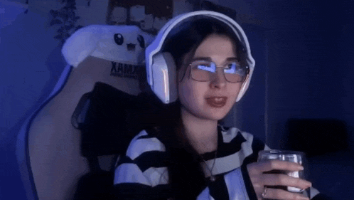 a woman wearing headphones and glasses is sitting in a chair and holding a glass of water .