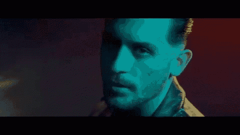 a man with a beard is wearing a leather jacket and looking at the camera in a dark room .