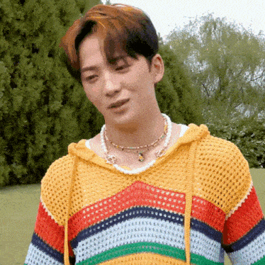 a young man wearing a rainbow colored sweater and a necklace