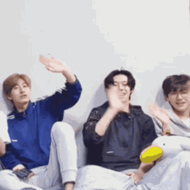 a group of young men are sitting on a couch and waving their hands .