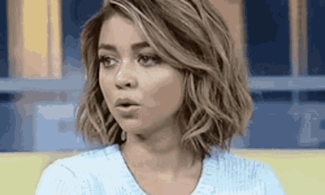 a woman with short wavy hair is wearing a blue sweater and making a funny face .