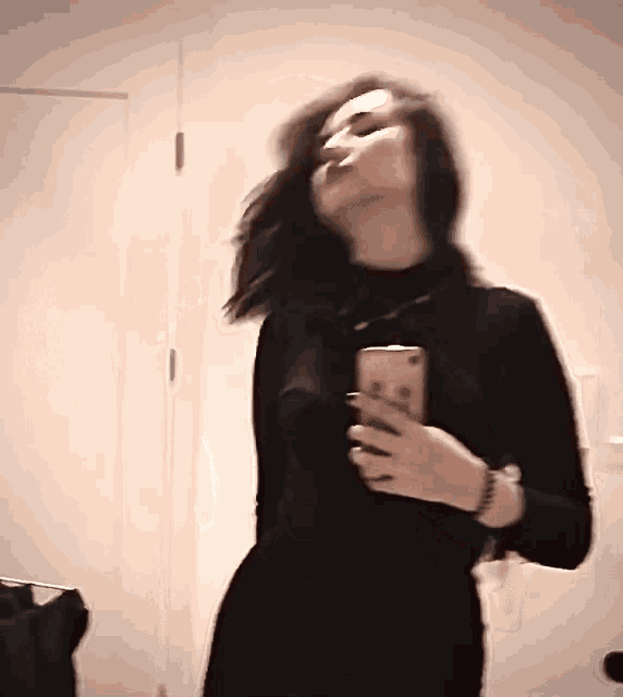 a woman in a black dress is taking a selfie in front of a mirror