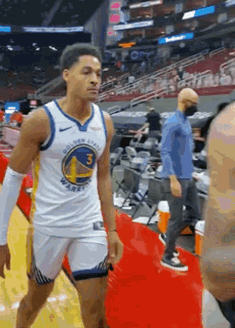 a man in a golden state warriors jersey is walking on the court .