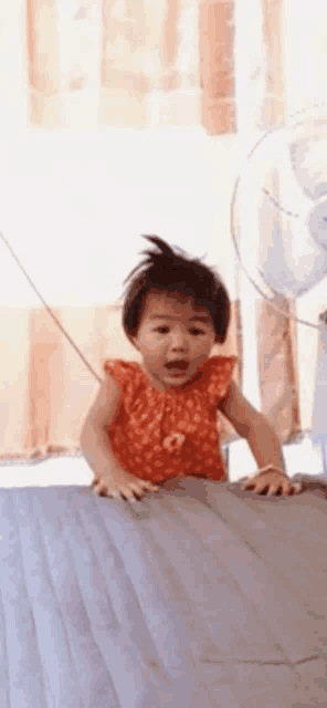 a little girl in an orange dress is crawling on a bed .