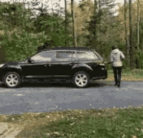 a black suv is parked on the side of the road with a woman walking towards it